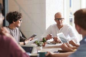 Man sat at a meeting table with other people.