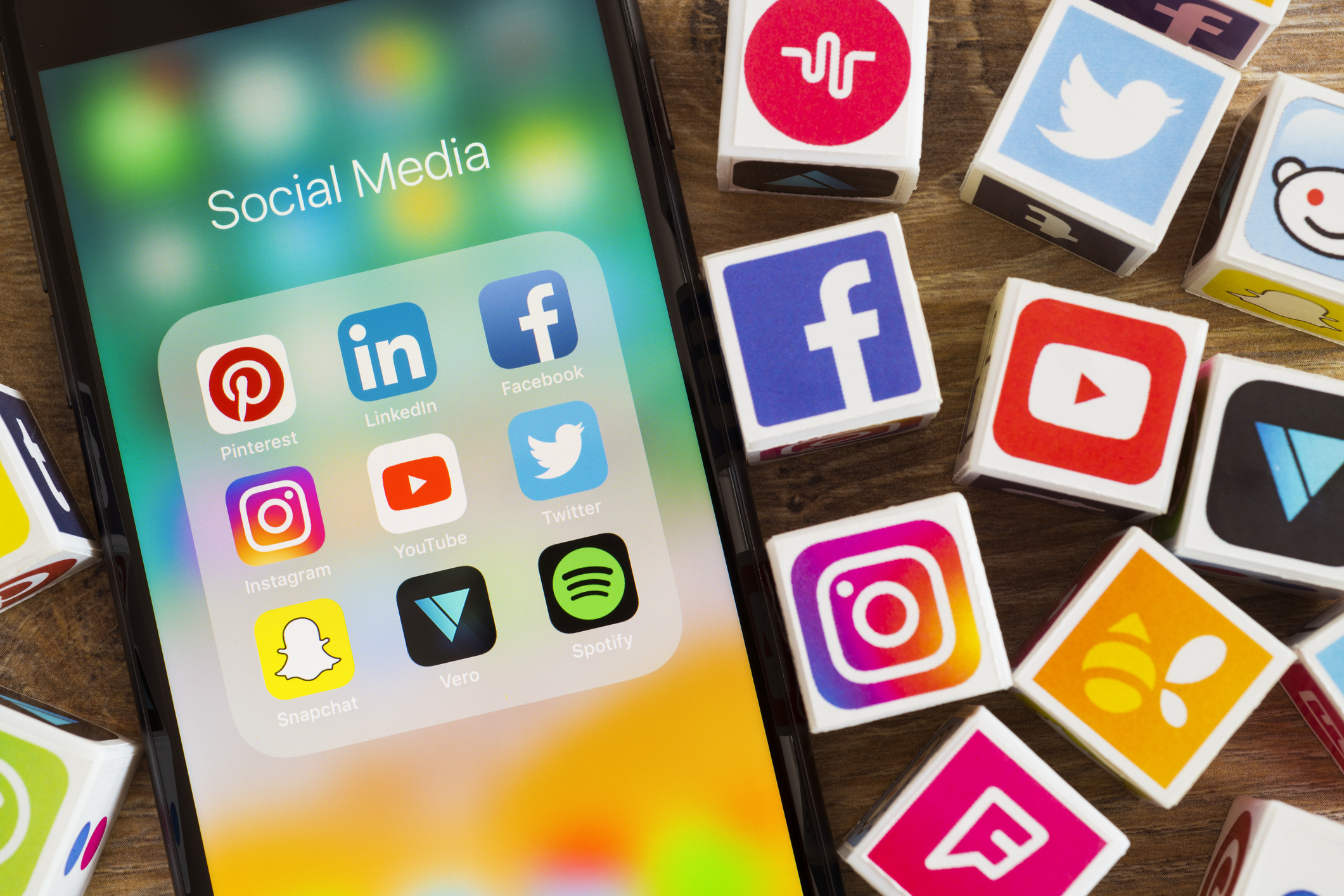 Plastic cubes with popular social media services icons, including Facebook, Instagram, Youtube, Twitter and an Apple iPhone 8 smart phone on an desk.