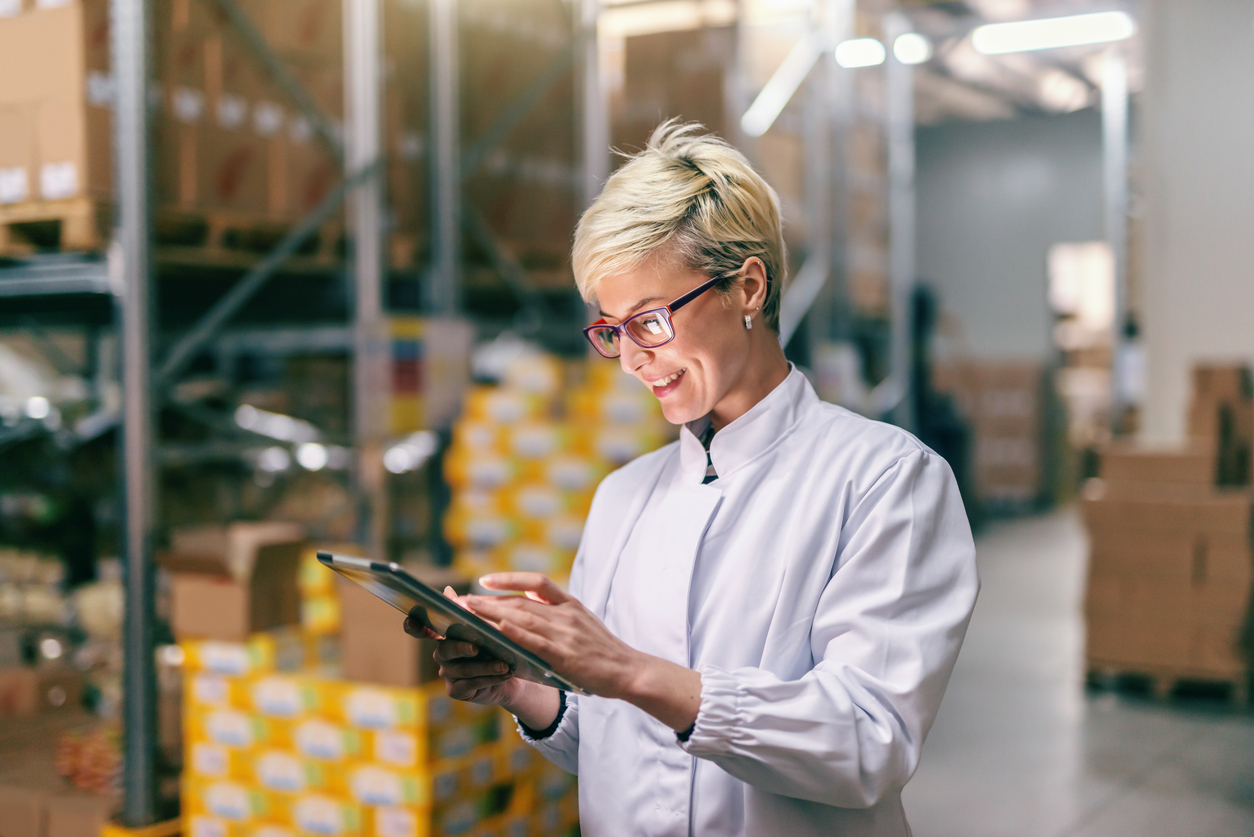 Woman in white uniform using tablet in warehouse.