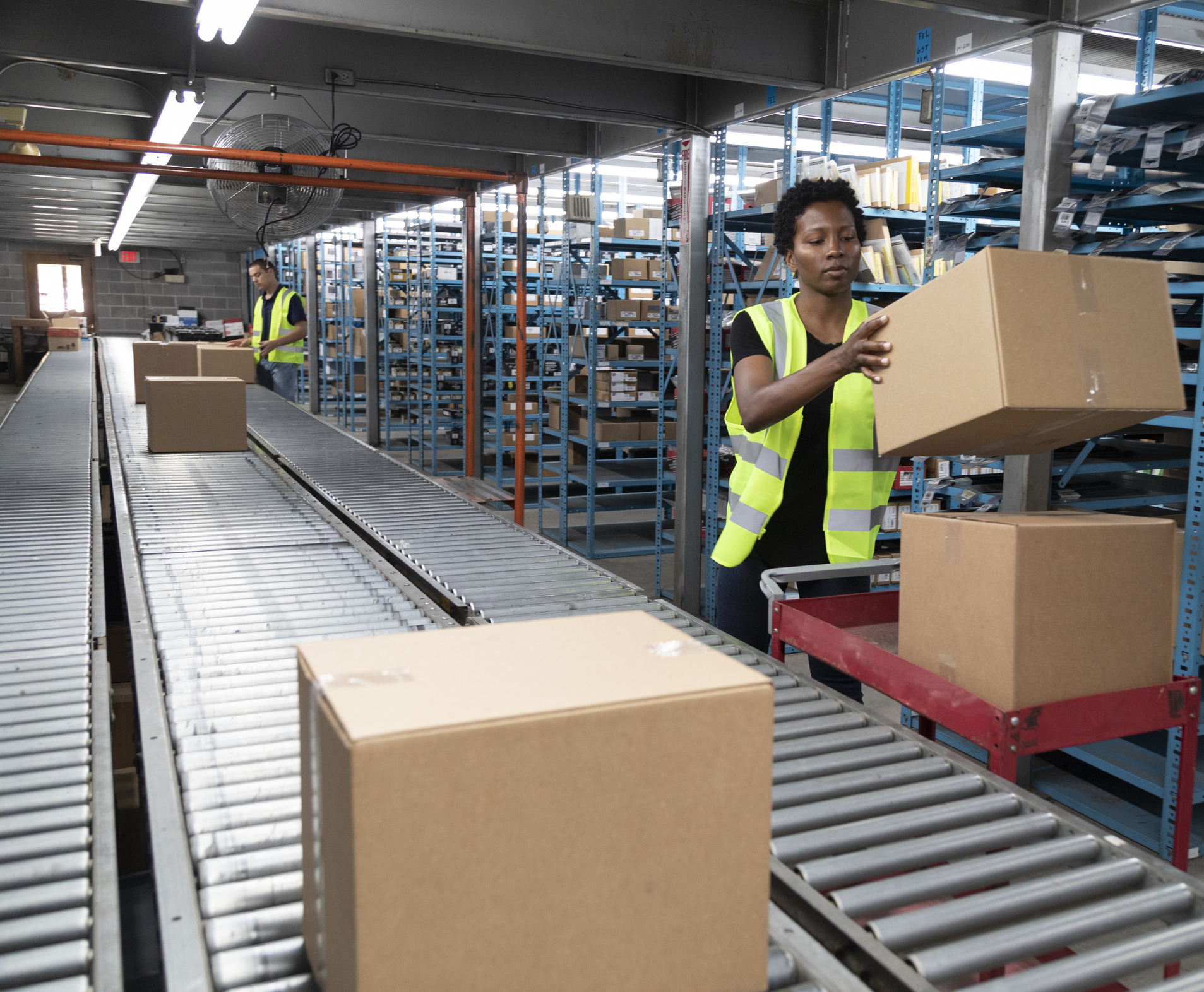 Two workers managing cardboard boxes on a conveyor belt.