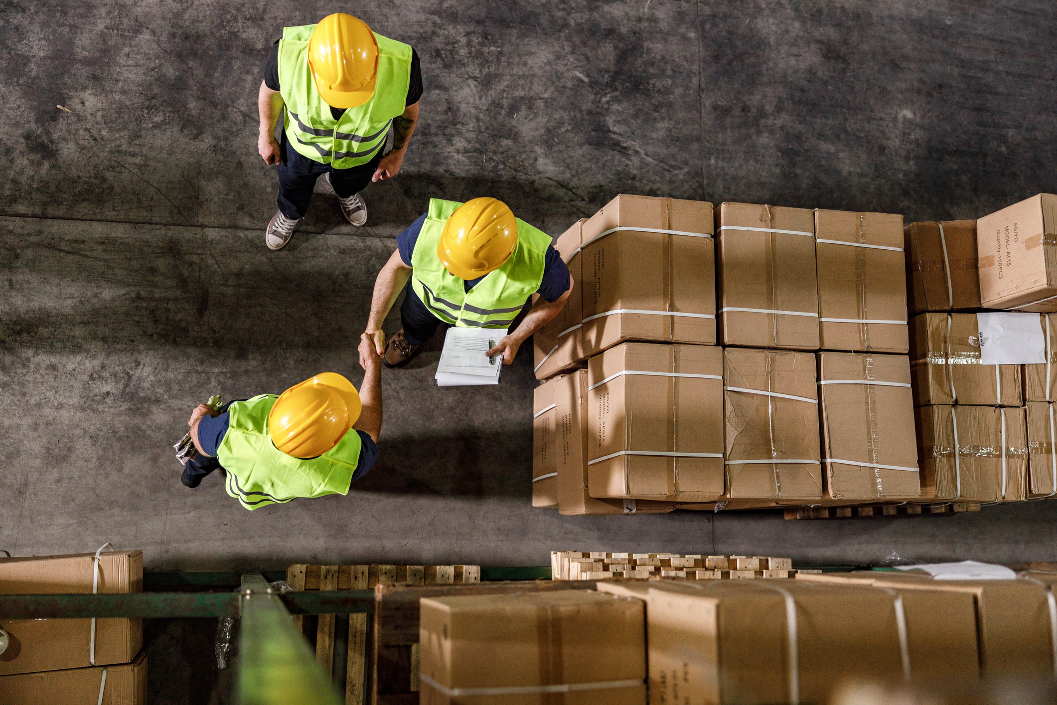 High angle view of two workers shaking hands while working with their colleague in distribution warehouse.