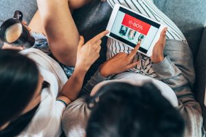 Two female friends drinking coffee and shopping online showing online discount