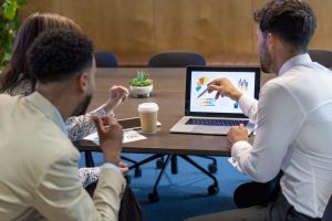Business colleagues are discussing data charts and graphs on a laptop computer. 