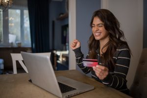 Happy woman sitting at her computer at the dining table having made a purchase online with her credit card