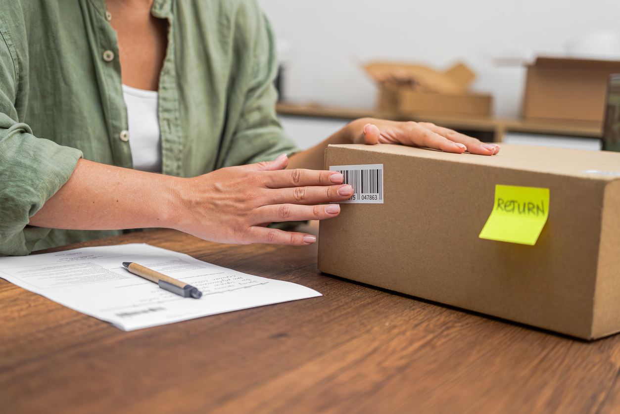 Hands of female consumer applies a return sticker on cardboard box with the concept of returning parcel.