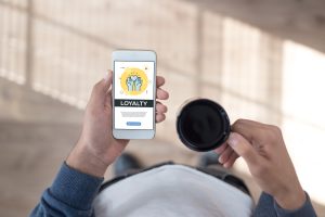 Man holding his phone in one hand and a cup of coffee in the other. Loyalty concept on mobile screen.